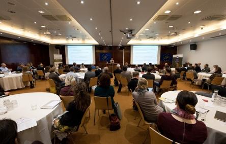 Foto toont de deelnemers aan de conferentie die een presentatie volgen
