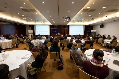 Foto toont de deelnemers aan de conferentie die een presentatie volgen