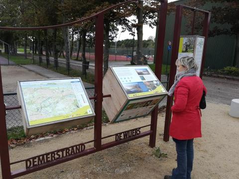 Vrouw kijkt naar de infoborden aan het Demerstrand